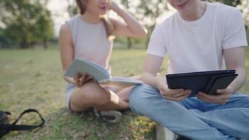 en suddig bild på digital surfplatta i mörkblått fodral med bakgrund av multietniska studenter som sitter och pratar och skrattar tillsammans i den gröna parken, bra brainstorming i lagarbete om projekt, natur och människor video