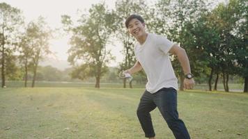 A cheerful overjoyed young adult inviting to play running together, slowly running on a green wide meadow inside natural park, taking off medical mask, hands reaching out with breathing gesturing video