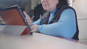 mulher idosa asiática usa óculos fazendo aprendizado on-line em casa, adulto maduro moderno usando dispositivo tablet portátil, pessoas e internet sem fio, planejamento de trabalho, educação a distância video