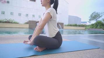 giovane donna asiatica che si china e si allunga per riscaldare il corpo prima di fare yoga sul tappetino, allungamento del corpo e delle gambe flessibili, tappetino da yoga, vitalità sana, piscina, controllo del respiro profondo e calmo video