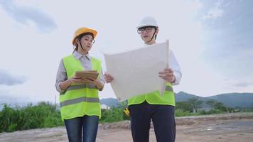 Low angle shot two workers analyzing a building safety project on a dirt construction site,  attractive female real estate agent using digital tablet to collect details, teamwork achievement concept video