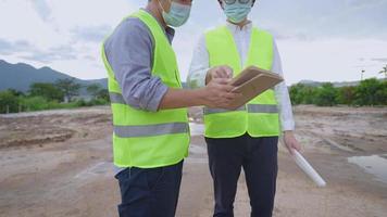 Asian engineer architect employee wear safety vest and safety helmet working together at construction outdoor site, holding tablet blueprints paper, teamwork solving problem, project work briefs, video