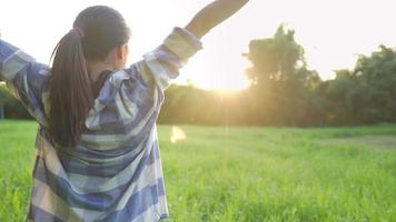 Young asian girl feeling happy and fresh standing on the green grass field enjoy warm morning light, good way to start a day, golden hour with sun light on the background, nature happiness sustainable video