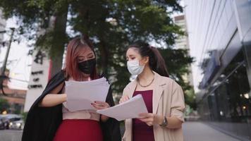Two hard working asian office workers weat surgical mask holding work paper walking and discuss project briefing, work pressure and stress, solving problem on working site, meeting preparation qa