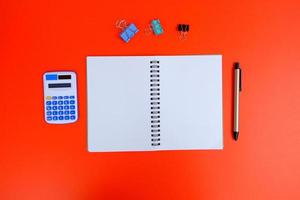 Blank notebook, a pen, and eyeglasses are on top of a white office desk table. Flat lay, top view. White designer office desk table with laptop, smartphone and supplies photo