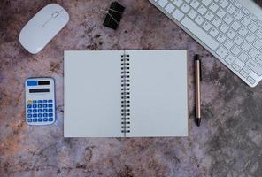 Blank notebook is in the middle of office desktable with pen and office supplies. Top view, flat lay. photo