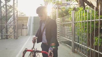 gelukkige jonge aziatische zakenman binnen met helm fietsen in de avond op de fiets manier in het groene stadspark, mooie zomerse sfeer en weerspiegeling van zonlicht als achtergrond, gezonde stadslevensstijlconcepten video