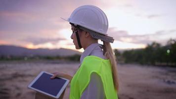 Portrait of young attractive female engineer closing tablet, looking at camera and take off safety hardhat, late finishing job, feeling relaxed stress relief, satisfied by project accomplishment video