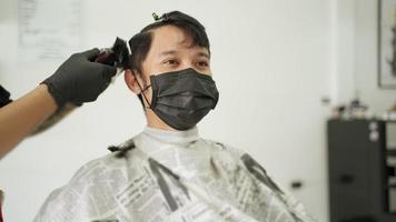 asiatisk man bär svart skyddsmask klipp av sig på manlig frisersalong. arbetande människor hårvård självförtroende. män hälsovårdsprodukt, corona virus pandemi covid-19 verksamhet öppnar igen video