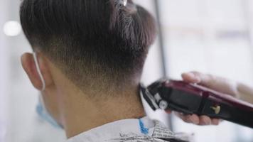 movimento de close-up do cabeleireiro corta o cabelo com máquina de cortar cabelo elétrica, vista traseira da cabeça do cliente jovem na reabertura do barbeiro, serviço de corte de cabeleireiro profissional bem-sucedido, atividades de autocuidado
