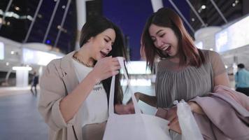 atractivas amigas asiáticas cerradas mostrando una mercancía en venta dentro de una bolsa de compras de tela, mujeres jóvenes alegres divirtiéndose y riéndose juntas, ropa femenina de moda, fin de semana de actividades de reunión