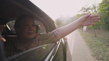 vrolijke senior geniet van een goed gevoel door landweg, oudere vrouw strekte haar hoofd uit uit bewegende auto met haar lange haar buiten de auto van het raam, geluk van pensioen