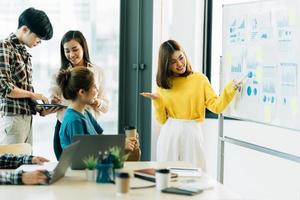 grupo de cuatro felices jóvenes compañeros de equipo de personas corporativas asiáticas que se reúnen para discutir negocios en la oficina. foto