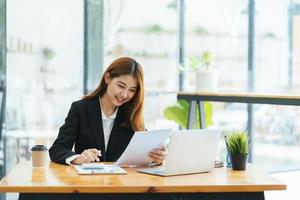 Portrait of Asian young female working on laptop and financial report at office. photo