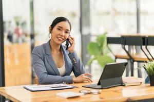 Asian businesswoman in formal suit in office happy and cheerful during using smartphone and working photo