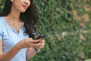 mujer asiática feliz sonriendo y sosteniendo el teléfono celular mientras se sienta en la cafetería de verano de la calle. foto