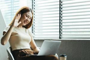 Asian woman having video call on her computer at home. Smiling girl studying online with teacher. photo