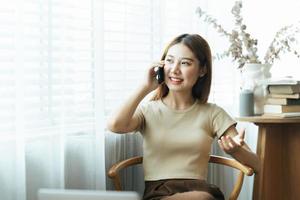 la mujer asiática con ropa informal es feliz y alegre mientras se comunica con su teléfono inteligente y trabaja en una cafetería. foto