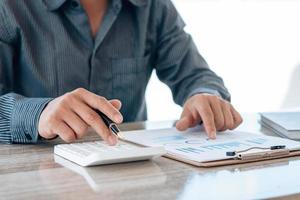 Close up hand of businessman or accountant hand holding pen working on calculator to calculate business data, accountancy document and laptop computer at office, business concept. photo