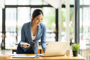 hermosa mujer asiática piensa ideas con computadora portátil en la cafetería foto