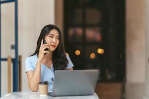 la mujer de negocios asiática con ropa informal de oficina es feliz y alegre mientras se comunica con su teléfono inteligente y trabaja en una cafetería. foto