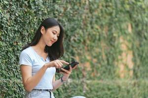 mujer asiática feliz sonriendo y sosteniendo el teléfono celular mientras se sienta en la cafetería de verano de la calle. foto