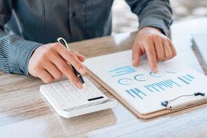 Close up hand of businessman or accountant hand holding pen working on calculator to calculate business data, accountancy document and laptop computer at office, business concept. photo