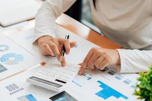 Close up hand of businessman or accountant hand holding pen working on calculator to calculate business data, accountancy document and laptop computer at office, business concept. photo