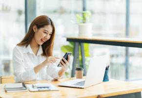 Asian woman in casual clothes is happy and cheerful while communicating with her smartphone and working in a coffee shop. photo