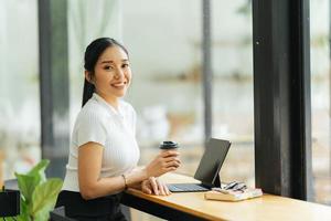 hermosa joven mujer de negocios asiática tomando café y usando una computadora portátil mientras trabaja en la oficina. foto