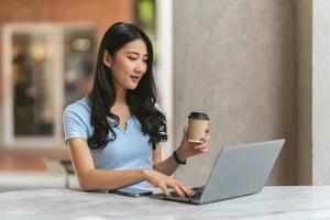 retrato de una joven asiática que trabaja en una laptop y un informe financiero en una cafetería.