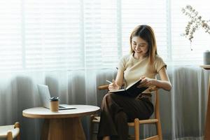 una joven mujer de negocios asiática está sentada en un escritorio y tomando notas en un cuaderno. el concepto de educación y tecnología. foto