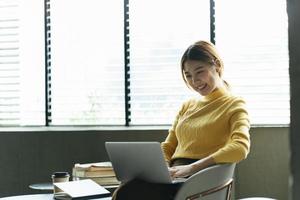 retrato de una hermosa mujer asiática sentada en el interior de un restaurante cafetería durante el verano, usando una computadora portátil y un teléfono inteligente con tecnología inalámbrica inteligente, relajándose en un café restaurante. foto