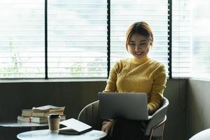 retrato de una hermosa mujer asiática sentada en el interior de un restaurante cafetería durante el verano, usando una computadora portátil y un teléfono inteligente con tecnología inalámbrica inteligente, relajándose en un café restaurante. foto