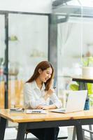 Portrait of Asian young female working on laptop and financial report at office. photo