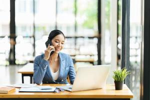 Asian businesswoman in formal suit in office happy and cheerful during using smartphone and working photo