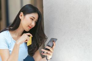 concepto de banca en línea. retrato de una joven asiática feliz con teléfono inteligente y tarjeta de crédito sentada en un café, mujeres asiáticas sonrientes disfrutando de hacer pagos desde casa.