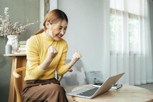 Young woman with laptop expressing excitement in home office, Excited Asian woman feel euphoric reading good news online. photo