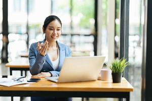 Asian female talking about sale report in video conference. Asian team using laptop and tablet online meeting in video call.Working from home remotely. photo