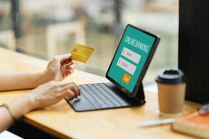 smiling woman paying online, using laptop, holding plastic credit card, sitting on coffee shop, Asian female shopping, making secure internet payment, browsing banking service. photo