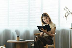 una joven mujer de negocios asiática está sentada en un escritorio y tomando notas en un cuaderno. el concepto de educación y tecnología. foto