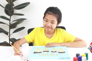 Creative girl sit on chair at the table drawing family picture. She smiles and painting with acrylic color. Happy family concept. Hobby at-home isolation in covid-19. photo