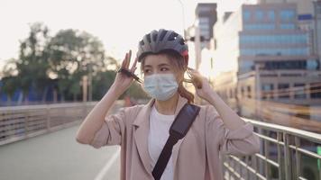 junge studentin trägt gesichtsmaske, die beim gehen auf der städtischen straße einen schutzhelm aufsetzt, geschäft in der innenstadt umwelt des alternativen verkehrskonzepts, vermeidet schlechte verkehrsluftverschmutzung