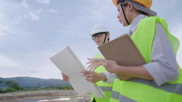 Asian young Engineer architecture wear safety vest helmet discuss on working project at construction site, specialist expertise working field, Real Estate investing, work gear tablet blueprints paper