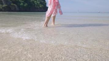 Low angle body part of Female walking on island water beach waves. pretty girl and splashing water ocean wave, summer vacation slow motion. Escape from busy polluted city life, travel destination