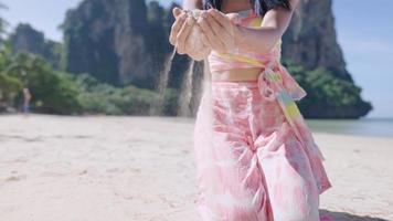 A young female hands holding a soft fine sand while sitting on summer beach, close up a motion of sand pouring down from female fingers, female tourist playing with sand on beach, beautiful coast view video