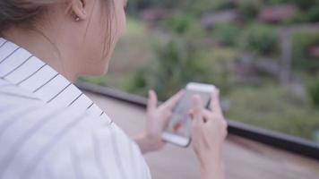 Young modern female with one small earing sitting on a natural cafe bench, sliding on application looks at friends activity and gossiping with other person next to her, technology and social activity video