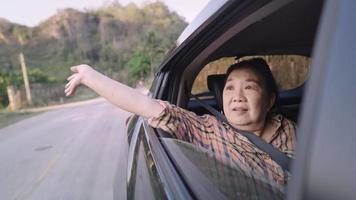 happy free retires woman sticking her hand out the car window, good health elderly touches the wind, enjoys view from the car journey window, freedom and happiness of retirement ages video