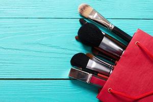 Makeup brushes on blue wooden background with copyspace. Make-up tools in red paper bag. Top view photo