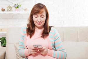 mujer morena de mediana edad, modelo de moda, usando ropa moderna, enviando mensajes de texto con su teléfono inteligente en el fondo. ama de casa. simular y copiar espacio foto